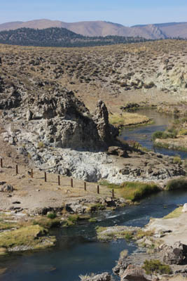 In flat rocky terrain, creek runs east next to a large rock outcropping.