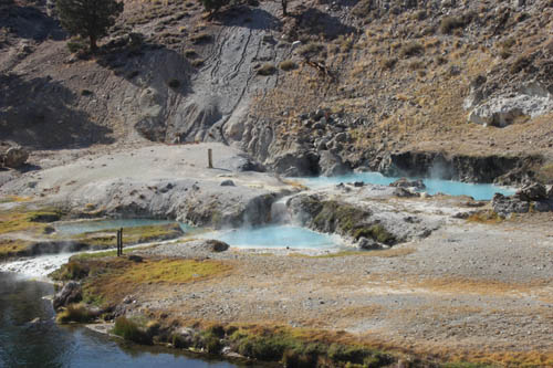 In a rocky terrain, three turquoise blue hot springs, steaming.