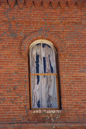 Ragged, spooky curtain on window in a red brick wall.