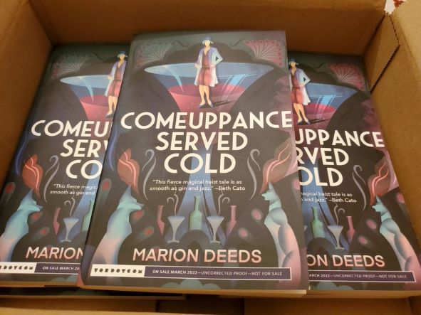 Five copies of Comeuppance Served Cold in a cardboard box.