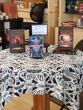 The Table. Raven and skeleton table cloth, black on white, l to r, Copper Road, Comeuppance Served Cold, Golden Rifts.