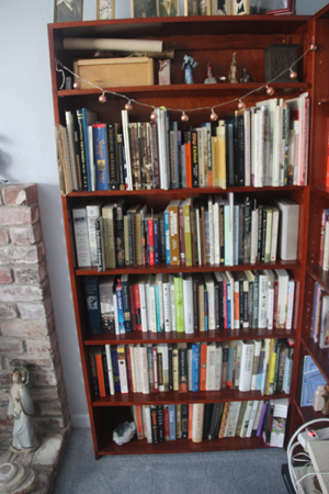 Five shelves of a bookcase, filled with nonfiction. Lower left, a Victoria Whitehand porcelain figure.