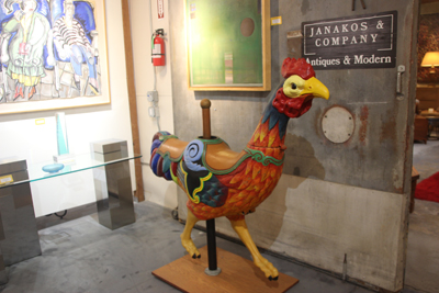 Large red and orange chicken carousel animal. Janakos and Company sign on the wall behind it.